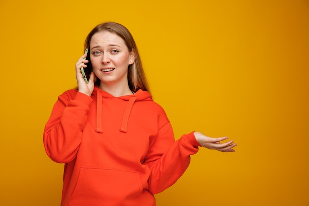 Clueless young blonde woman showing empty hand talking on phone 