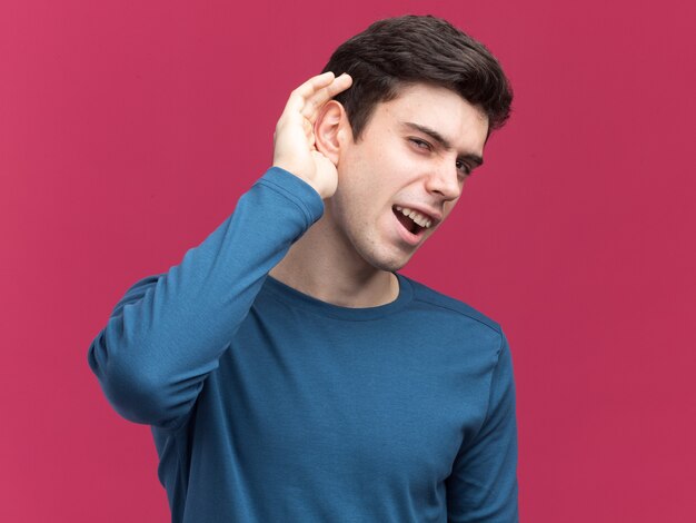 Clueless young brunette caucasian boy holds hand behind ear trying to head on pink