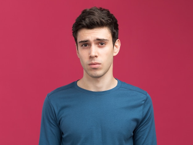 Clueless young brunette caucasian boy looking at camera on pink