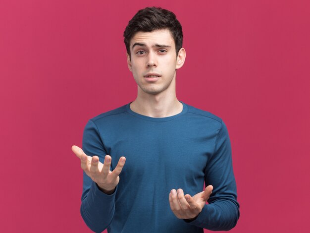 Clueless young brunette caucasian boy looking and pointing at camera with hands on pink