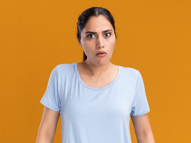 Clueless young brunette caucasian girl looking at camera on orange