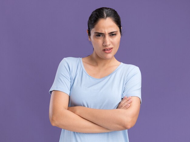 Clueless young brunette caucasian girl standing with crossed arms on purple