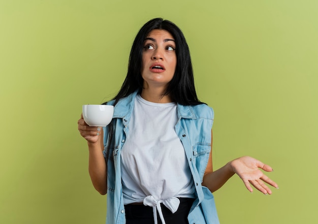 Clueless young caucasian woman holds cup and looks at side