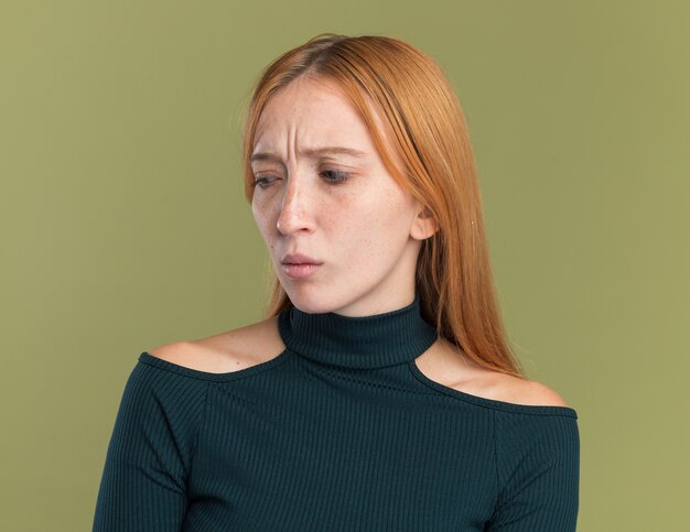 Clueless young redhead ginger girl with freckles looking at side on olive green