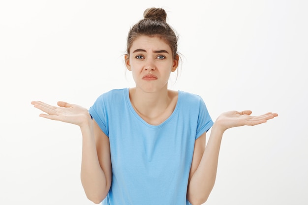 Clueless young woman shrugging and grimacing unaware, don't know anything