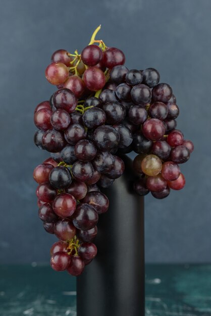 A cluster of black grapes around a bottle on marble table.