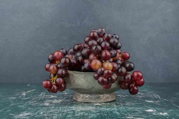 A cluster of black grapes in the vase on marble table.
