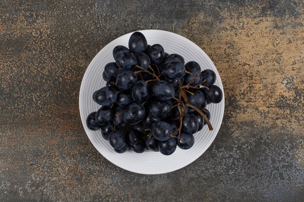Cluster of black grapes on white plate.