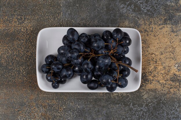 Cluster of black grapes on white plate. 