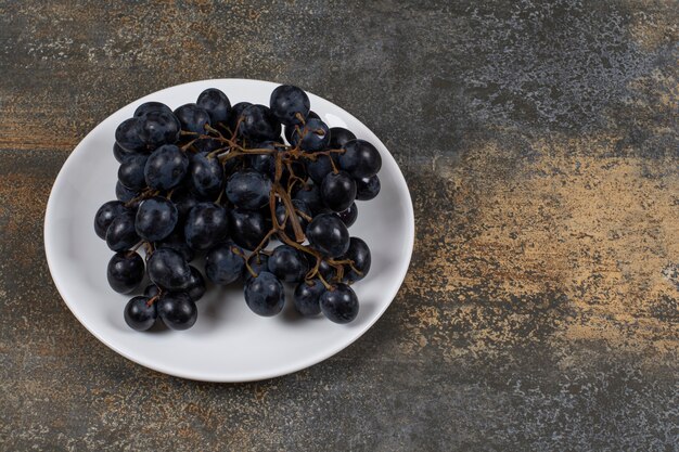 Cluster of black grapes on white plate.