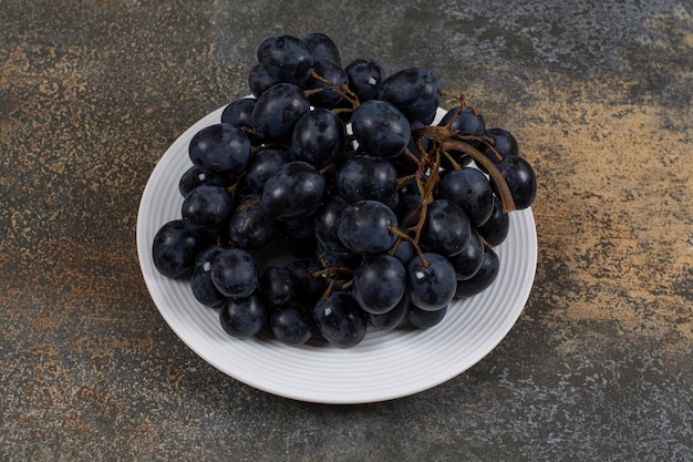 Гроздь черного винограда на белой тарелке.