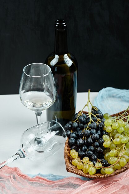 A cluster of mixed grapes in basket and glasses of wine and bottle with pink and blue tablecloth. High quality photo