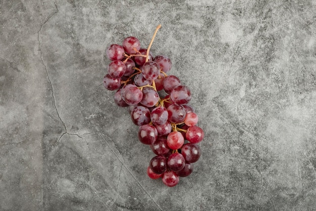 Гроздь красных свежих спелых виноградин на мраморной поверхности.
