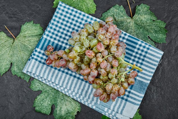 A cluster of red grapes with leaves and blue tablecloth on dark background. High quality photo