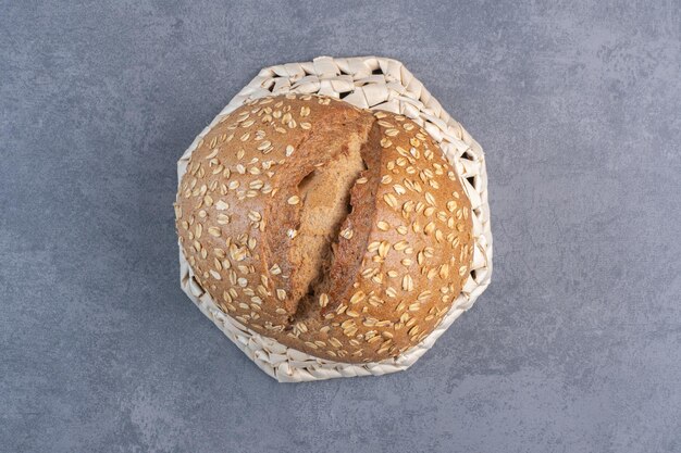 Coating of flakes on a loaf of bread on an upside-down basket on marble background. High quality photo