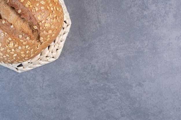 Coating of flakes on a loaf of bread on an upside-down basket on marble background. High quality photo