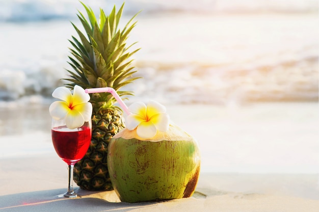 Cocktail glasses with coconut and pineapple on clean sand beach - fruit and drink on sea beach