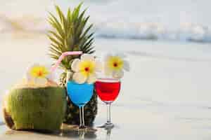 Free photo cocktail glasses with coconut and pineapple on clean sand beach - fruit and drink on sea beach