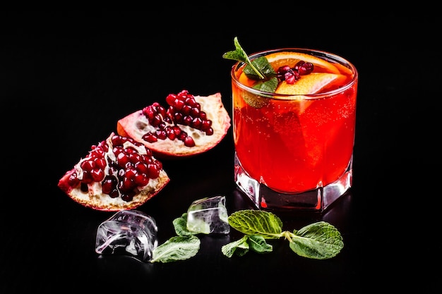Foto gratuita cocktail di vodka, granatina, melograno, ghiaccio e menta si erge su un tavolo nero
