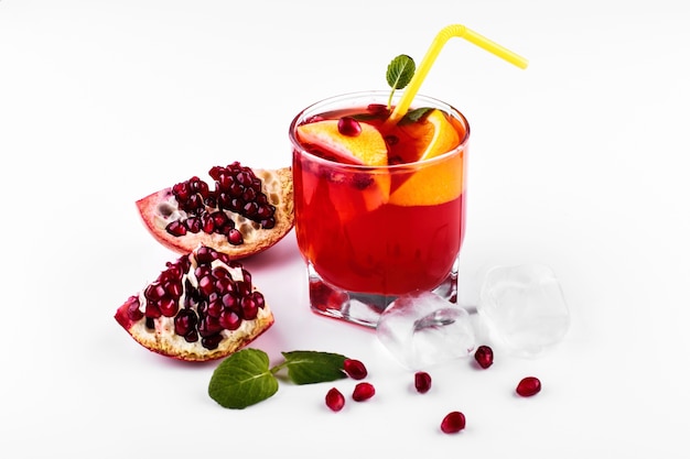 Cocktail of vodka, grenadine, pomegranate, ice and mint stands on a white table