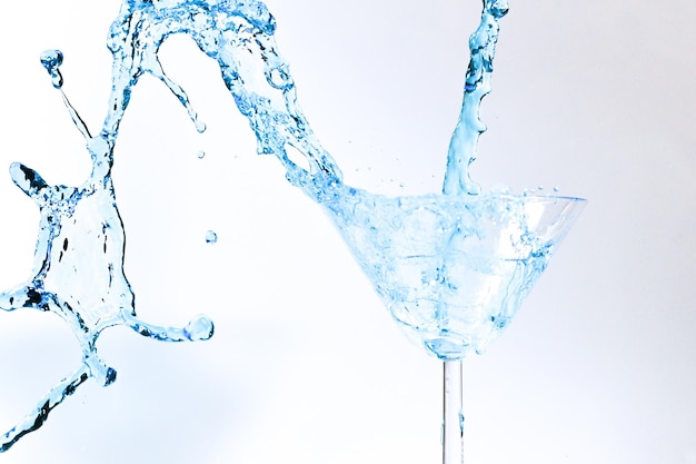 Коктейль с синей жидкостью в стакане. стекло с голубой водой, наливаемой жидкостью с брызгами и каплями. бокал мартини с алкоголем с брызгами на белом фоне. концепция освежающего напитка.