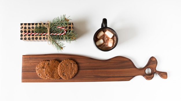 Cocoa cup near wrapped gift and board with cookies