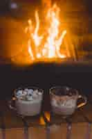 Free photo cocoa mugs with marshmallows near the fireplace.