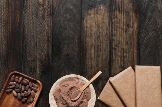 Cocoa powder and beans with wrapped chocolate bar on wooden table