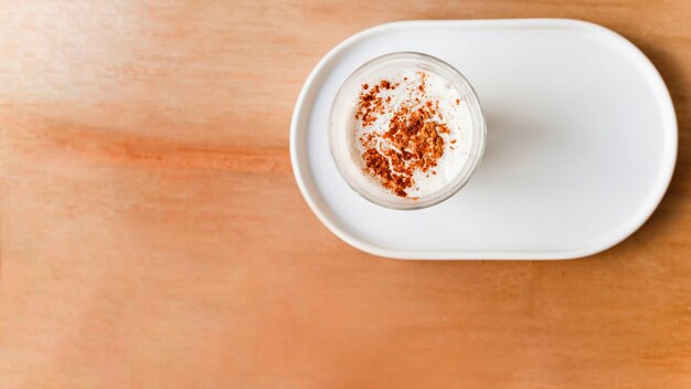 Cocoa powder over the coffee glass on tray over the brown textured backdrop