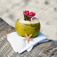 Foto gratuita cocktail di cocco con cannuccia su una palma in spiaggia