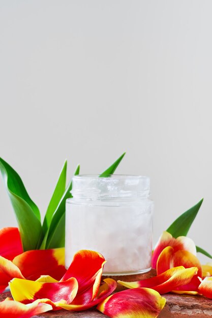 Coconut oil in a jar on white surrounded by tulip petals, close-up with copy space