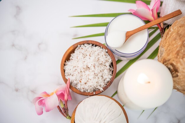 Coconut oil, tropical leaves and fresh coconuts. Spa coconut products on light wooden surface.