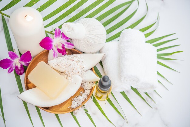 Coconut oil, tropical leaves and fresh coconuts. Spa coconut products on light wooden surface.