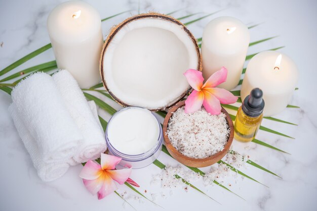 Coconut oil, tropical leaves and fresh coconuts. Spa coconut products on light wooden surface.