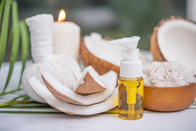 Coconut oil, tropical leaves and fresh coconuts. Spa coconut products on light wooden surface.