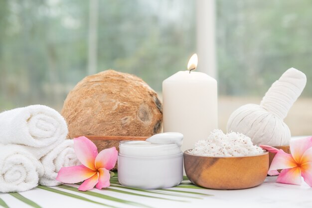 Coconut oil, tropical leaves and fresh coconuts. Spa coconut products on light wooden surface.