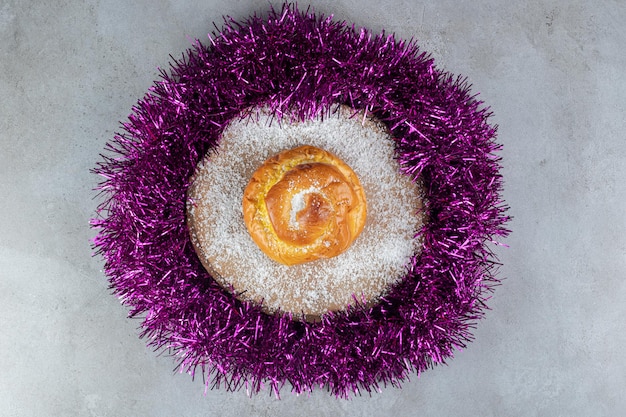 Foto gratuita sottopentola ricoperta di polvere di cocco con un panino in un cerchio di ghirlanda su una superficie di marmo