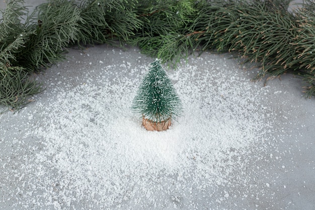 Coconut powder pile under tree figurine, in front of pine branches on marble surface