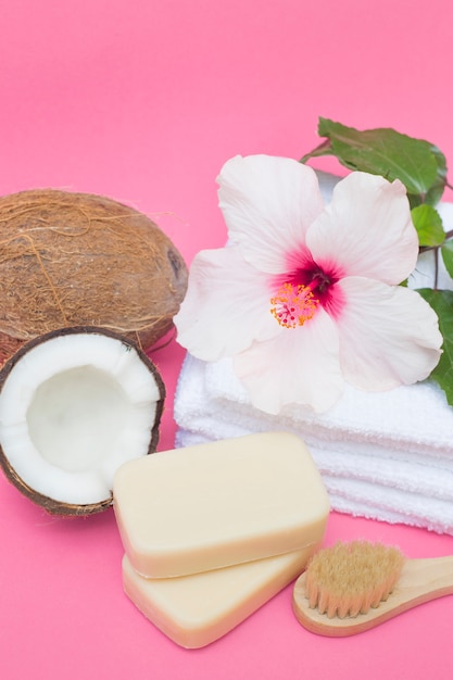 Noce di cocco; sapone; spazzola; fiore e asciugamani sulla superficie rosa