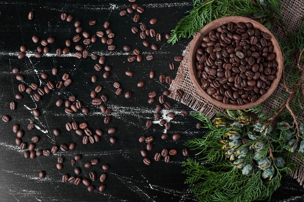 Кофейные зерна на черном фоне в деревянной чашке.