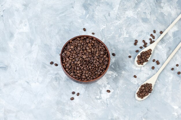 Coffee beans in bowl and wooden spoons top view on a grey plaster background