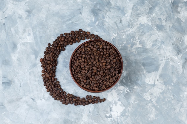 Coffee beans in a clay bowl on a grey plaster background. top view.