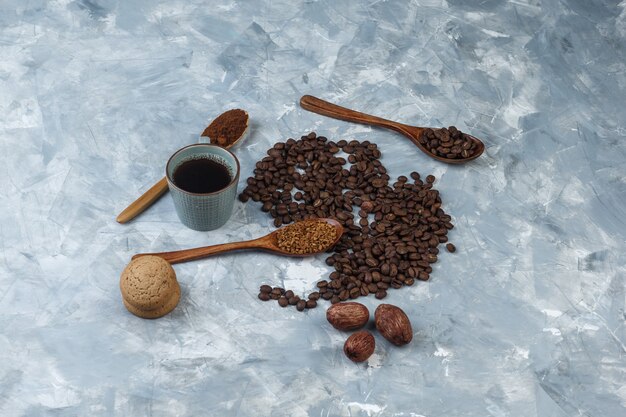 Кофейные зерна, чашка кофе с растворимым кофе, кофейная мука, кофейные зерна в деревянных ложках, вид печенья под высоким углом на светло-синем мраморном фоне