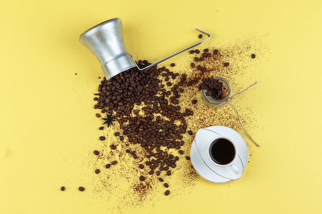 Coffee beans in a jug with glass jar, cup of coffee flat lay on a yellow background