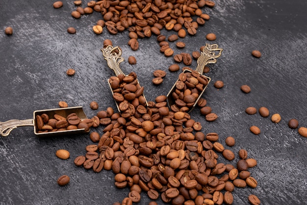 coffee beans in metal spoon on dark surface