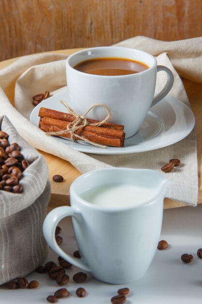자루, 우유, 마른 계 피, 플랫폼 및 흰색 테이블에 커피 한 잔에 커피 콩. 측면보기.