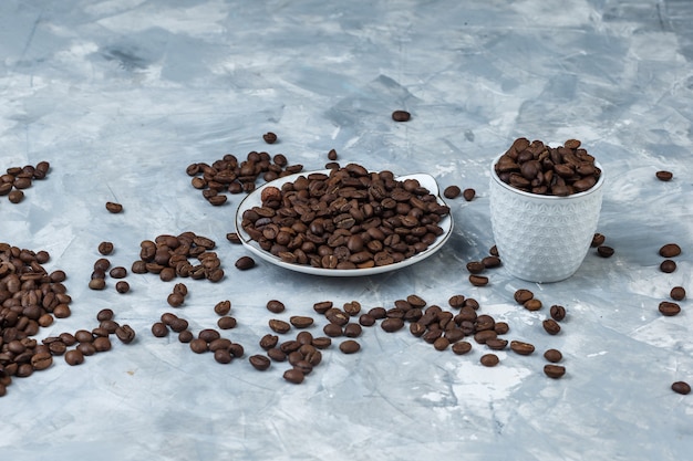 Coffee beans in white cup and plate on a grey plaster background. high angle view.