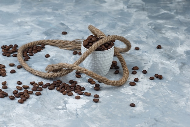 Coffee beans in a white cup with rope high angle view on a grey plaster background