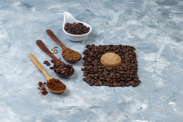 Кофейные зерна в белом фарфоровом кувшине с кофейными зернами, растворимым кофе, кофейной мукой в деревянных ложках с высоким углом обзора на светло-синем мраморном фоне