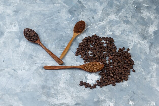 Coffee beans with instant coffee, coffee flour, coffee beans in wooden spoons close-up on a light blue marble background